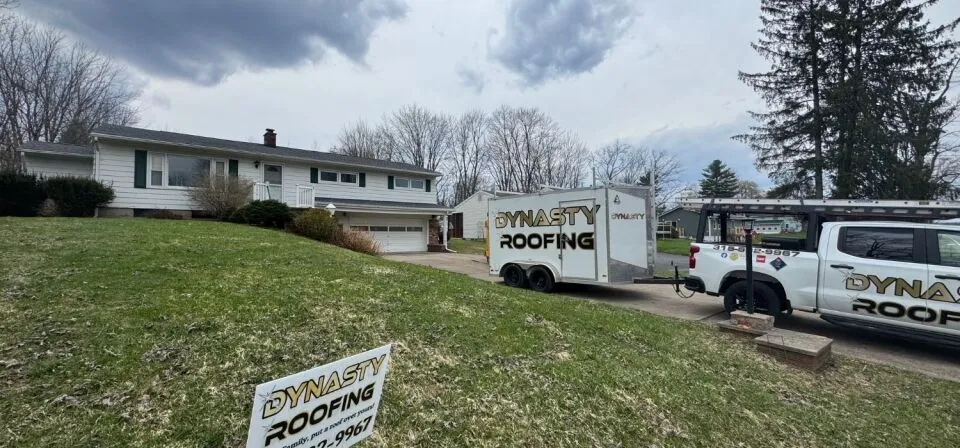 Dynasty Roofing truck, trailer, and yard sign parked outside a residential home during a roofing project in a suburban neighborhood.