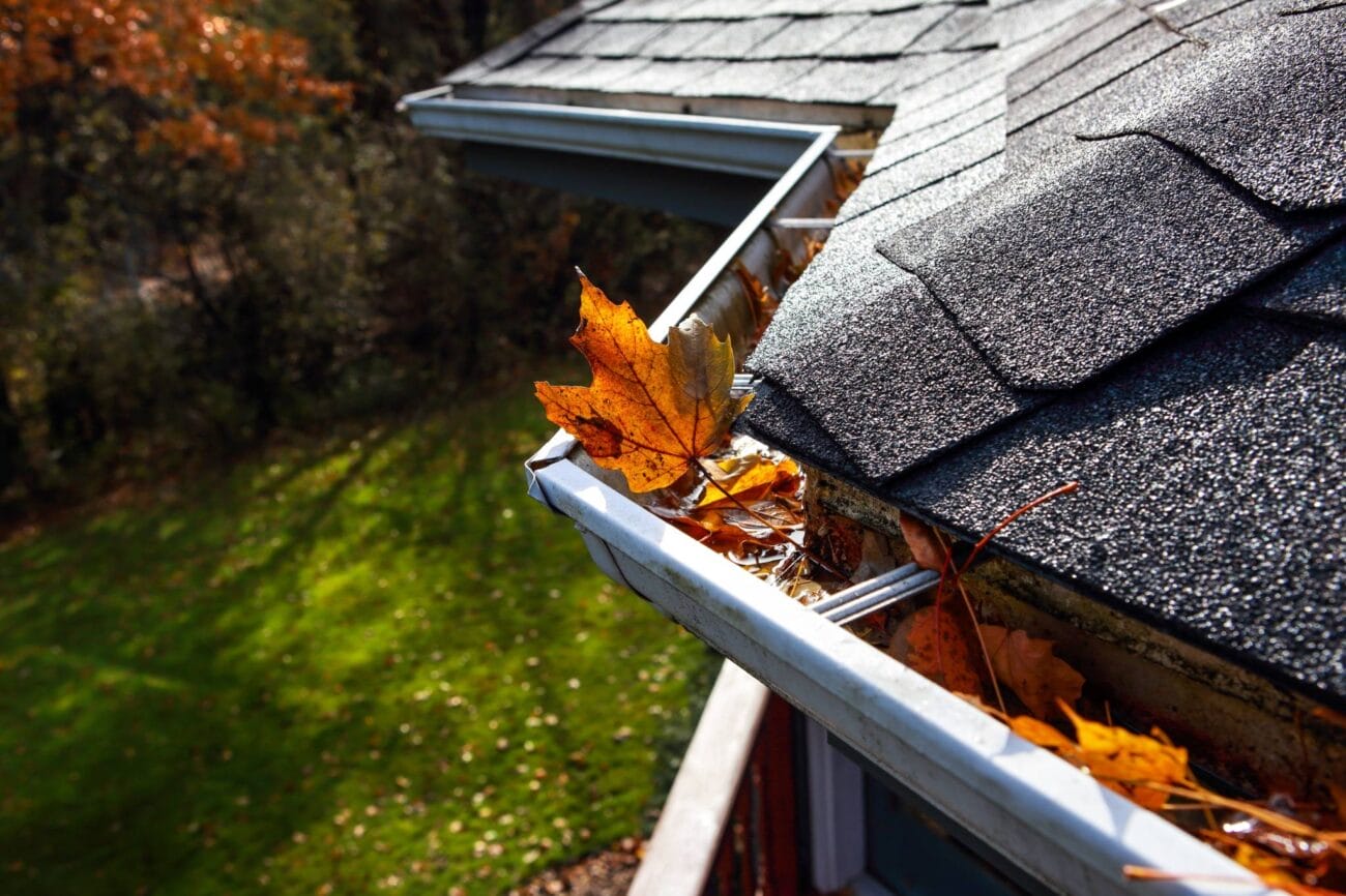 A clogged gutter filled with autumn leaves highlights the importance of fall roof maintenance to prevent water damage.
