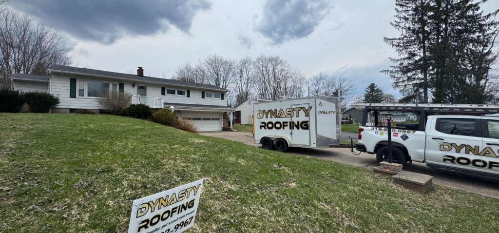 Dynasty Roofing truck, trailer, and yard sign parked outside a residential home during a roofing project in a suburban neighborhood.